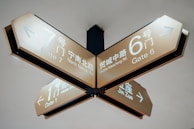 A ceiling-mounted directional sign in a public space displays information in both Chinese and English. The sign points to different gates and nearby roads, with gates numbered 6, 7, and 1, directing towards Gate 6, Gate 7, and Gate 1. The roads mentioned are Middle Maocheng Rd., North Ninnan Rd., and Middle Simen Rd.