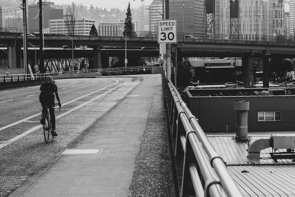 橋の上を自転車で走る人のグレースケール写真