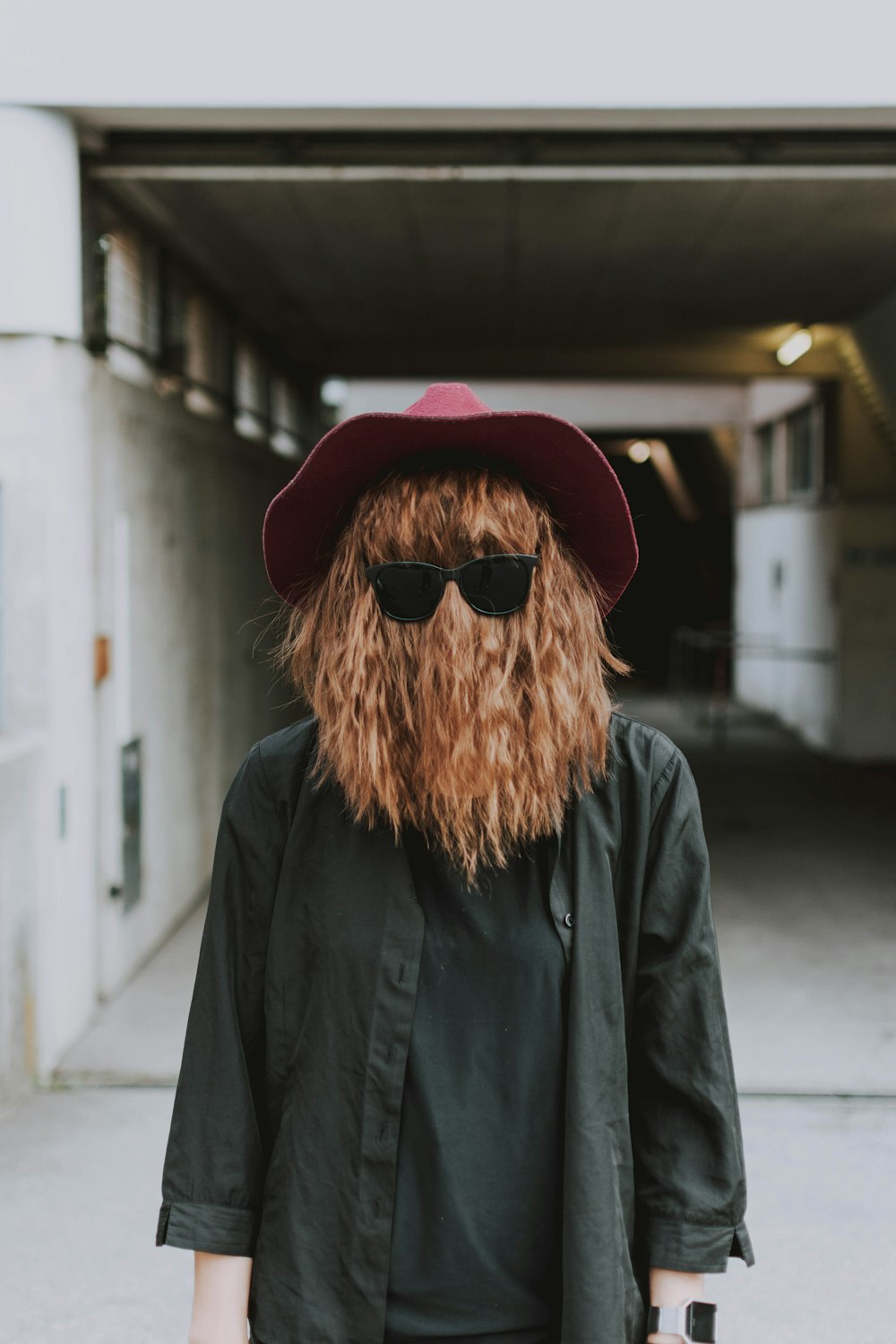 Person, die Gesicht mit Haaren bedeckt, während sie Sonnenbrille und graues Hemd trägt