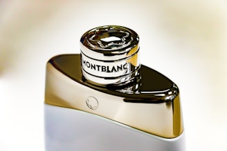 A sleek, metallic Montblanc perfume bottle with a reflective surface and a distinct circular emblem on the cap, set against a neutral background.