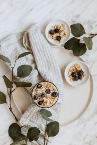 A stylish flat lay of a healthy breakfast with fresh fruit, a notebook, and a pink water bottle on a soft off-white surface.