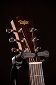Close-up of a guitar's headstock with tuning pegs and strings, featuring a logo and mounted on a stand against a dark background.
