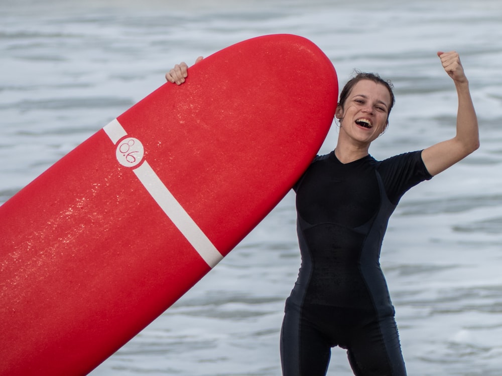 woman standing on shore raising her surfboard