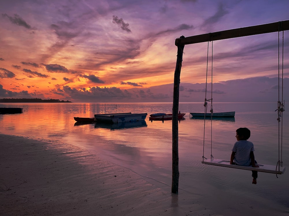 boy sitting on swing chair near body of water