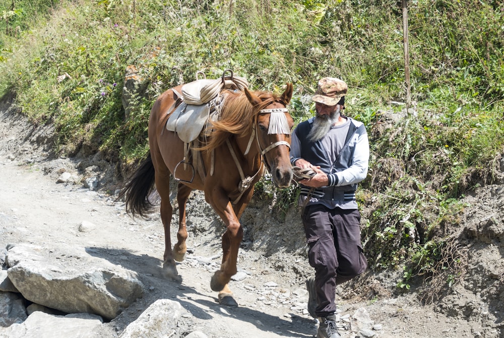 person holding brown horse near dirt road during daytime