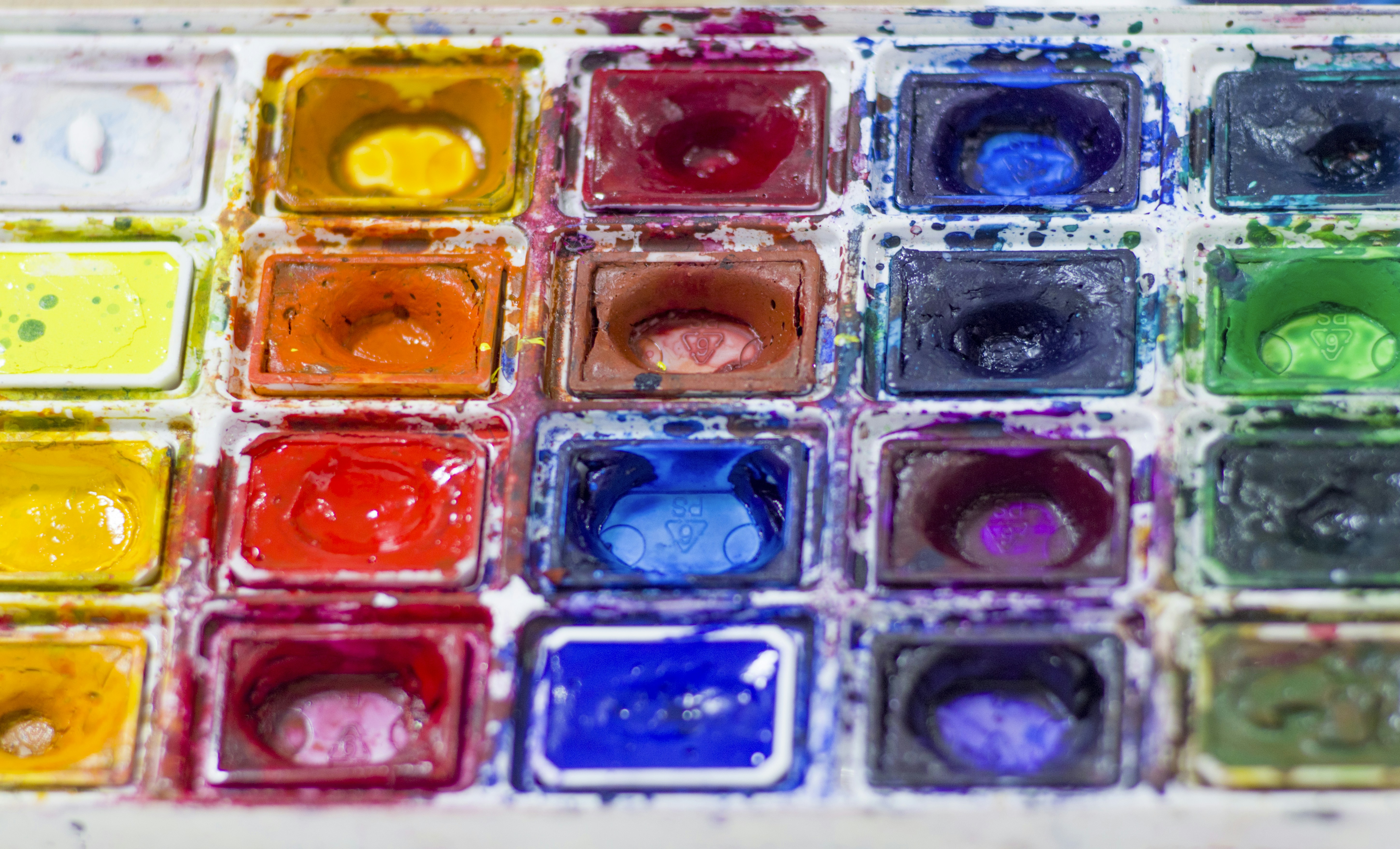 Bir ressamın palet üzerinde farklı renklerdeki boyaları fırça ile karıştırarak yeni tonlar elde etmesini gösteren yakın çekim sanatsal görsel.