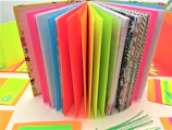 An open scrapbook showing layered collages of pastel papers, textured elements, and charming handwritten notes.