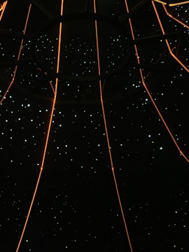 A dark space filled with small star-like lights scattered throughout, intersected by glowing orange lines that converge at a central circular structure.