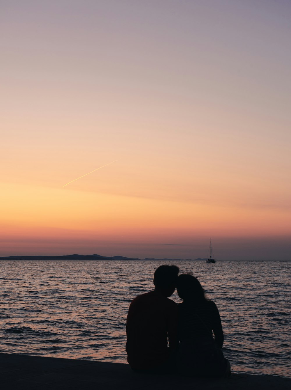 Silhouette eines Mannes und einer Frau, die während des Sonnenuntergangs in der Nähe eines Gewässers sitzen