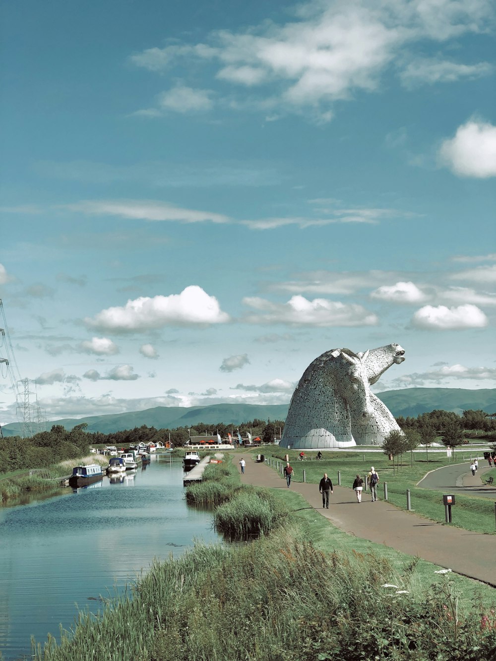 people walking near park viewing lake under blue and white skies