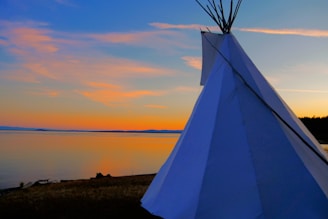 Sunset over a warm, inviting teepee nestled in rolling green hills with a family playing nearby.