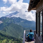 woman sitting on wooden dock front of mountain at daytime