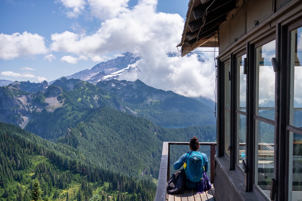 woman sitting on wooden dock front of mountain at daytime