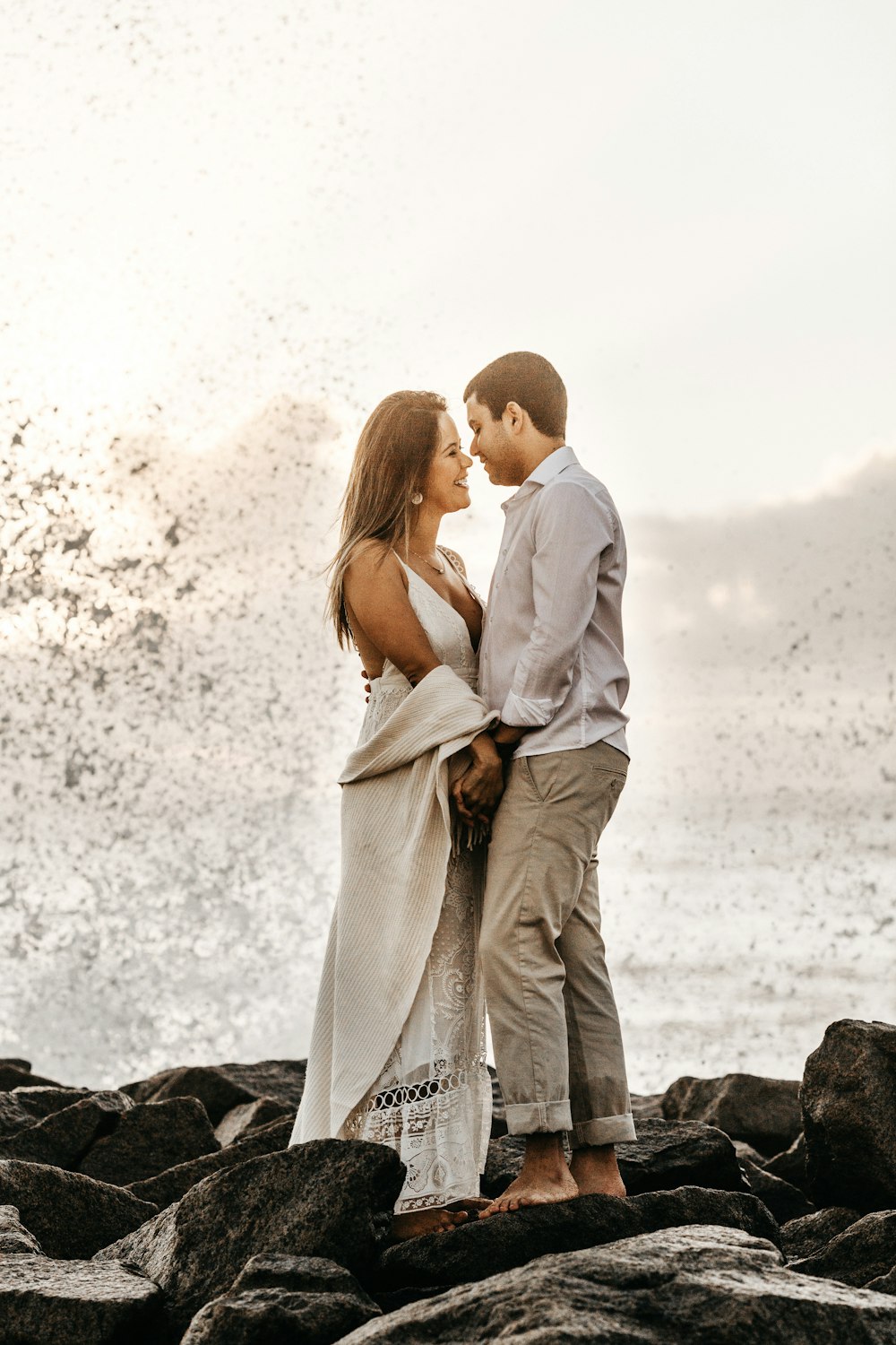 man and woman facing each other while standing on rock boulders in seashore