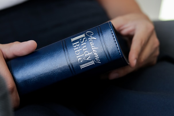 A close-up of hands holding a printed Revelation Bible Study book with classic slate blue accents.