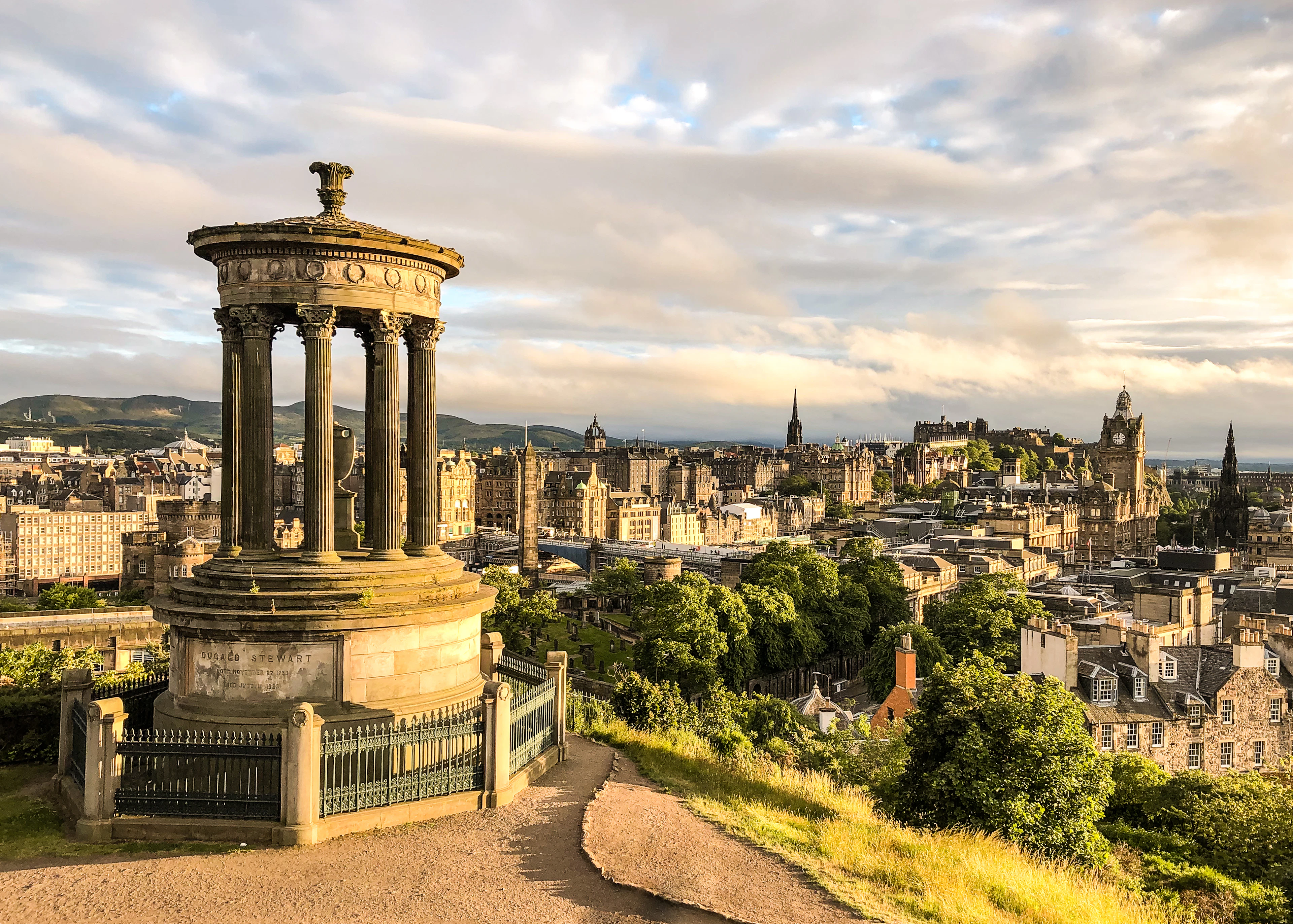 The Dugald Stewart Monument overlooks Edinburgh's rooftops in warm evening light.