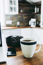 A cozy kitchen corner with a smartphone displaying the WhiskWhere app and a cup of coffee nearby.