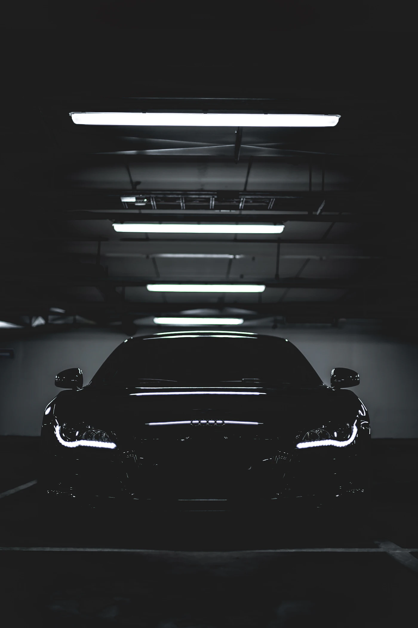 A glossy dark sports car under rows of garage lights