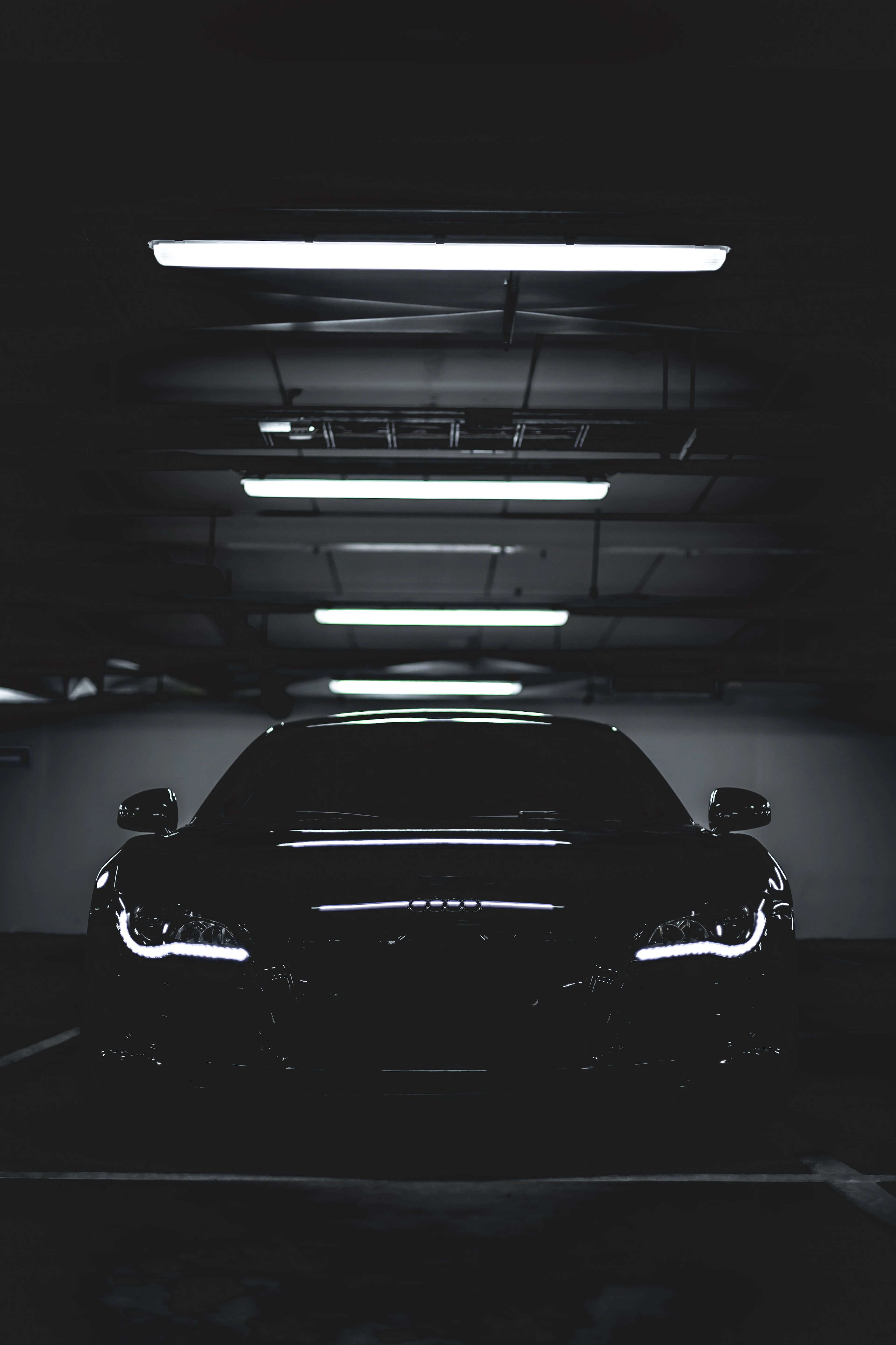 Carro preto estacionado em uma garagem escura sob faixas de luz