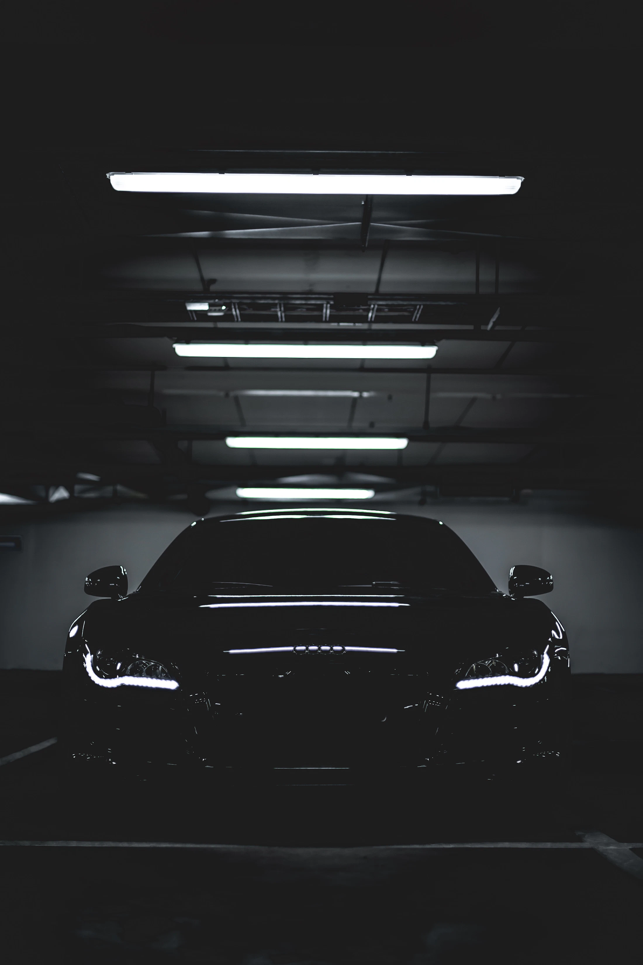 A black car parked under overhead lights in a dark garage