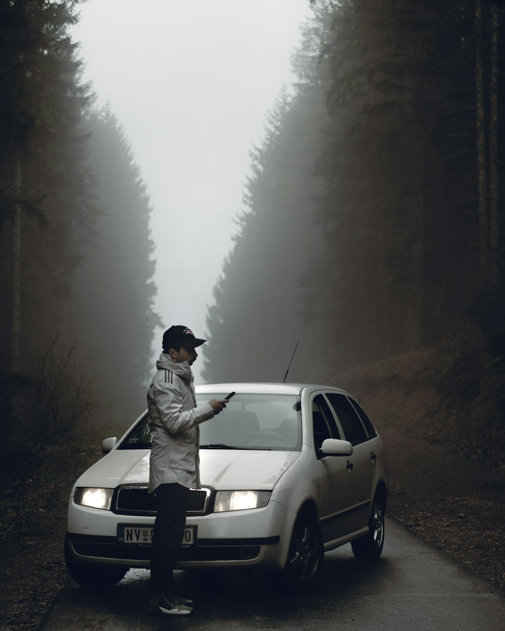 grayscale photography of man standing in front of Skoda hatchback