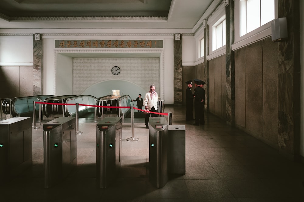 three soldier men standing near pathway and another woman walking going on escalator inside building