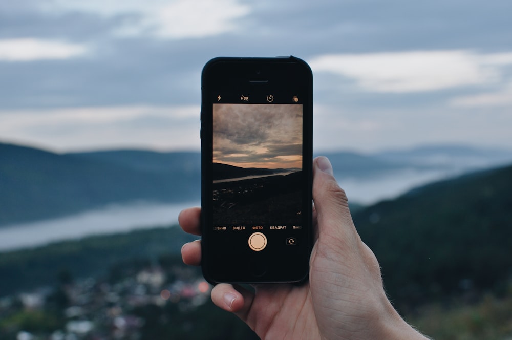person holding iPhone capturing mountain