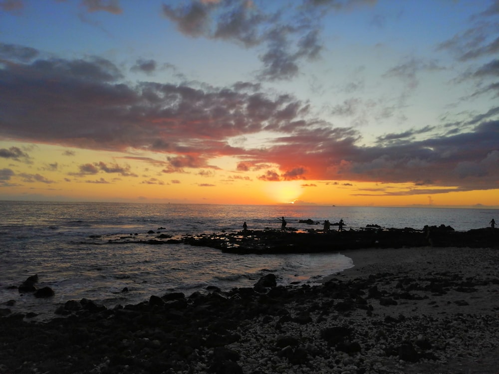 several people standing on rock boulders in shore during golden hour