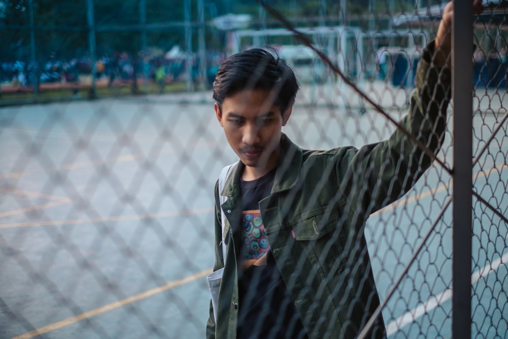 man in black button-up jacket behind chain-linked fence