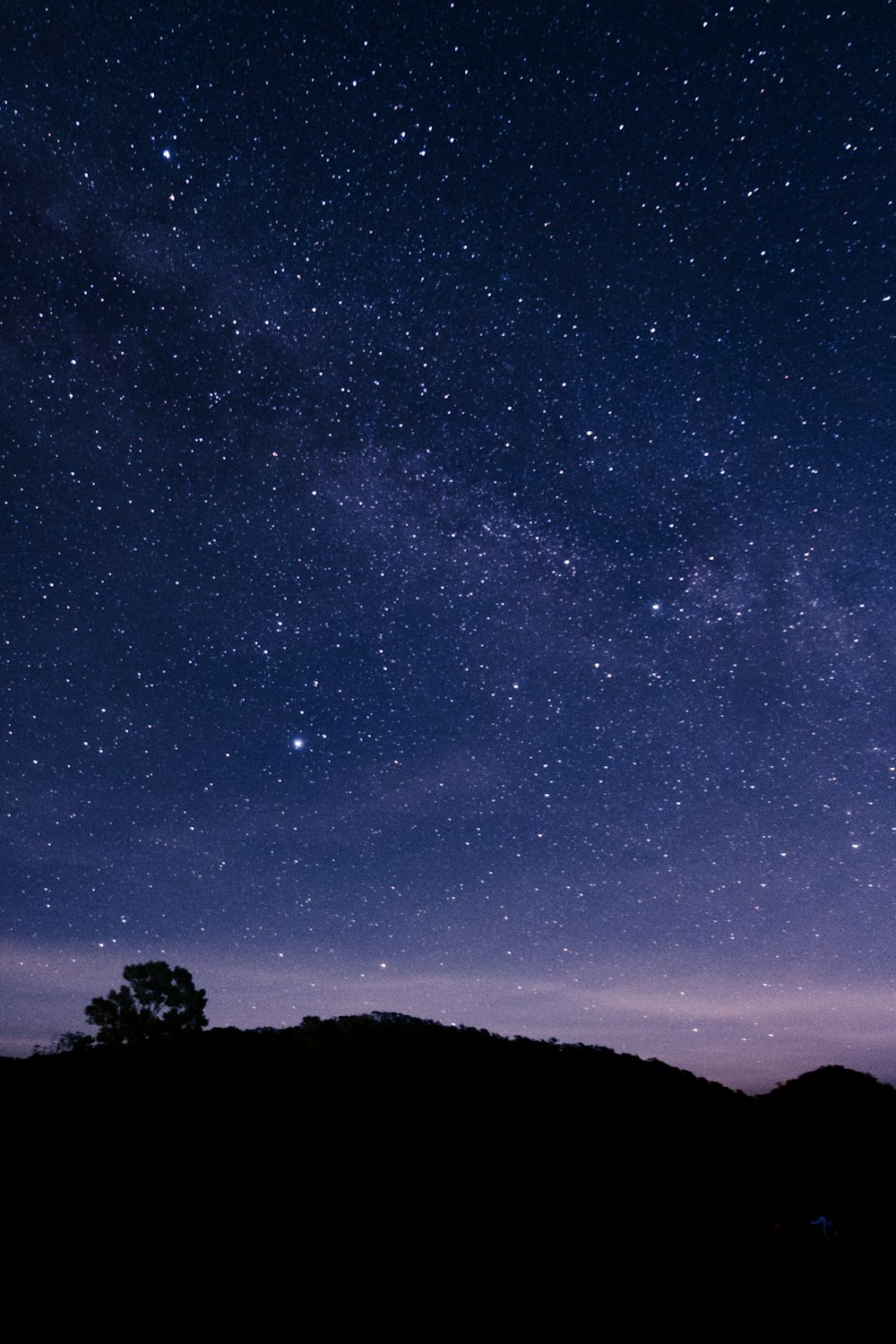 the night sky is filled with stars above a hill