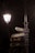 A street lamp illuminates a metal signpost at night. The signpost has several directional signs pointing to locations such as 'U.S. Club', 'Rani Jhansi Park', 'Mall Road', and 'Lift'. The background is dimly lit, with shadows and faint outlines of trees.