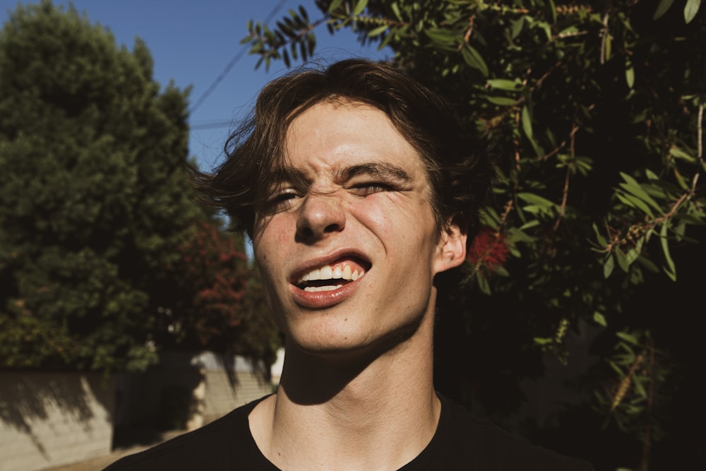 man winking and smiling in front of green leaves