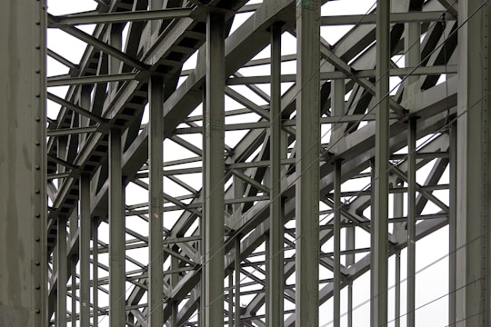 A complex metallic structure with numerous intersecting beams and rivets, creating a pattern of lines and angles. The beams display metalwork typical of industrial or infrastructure constructions.