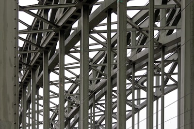 A complex metallic structure with numerous intersecting beams and rivets, creating a pattern of lines and angles. The beams display metalwork typical of industrial or infrastructure constructions.