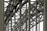 A complex metallic structure with numerous intersecting beams and rivets, creating a pattern of lines and angles. The beams display metalwork typical of industrial or infrastructure constructions.