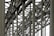 A complex metallic structure with numerous intersecting beams and rivets, creating a pattern of lines and angles. The beams display metalwork typical of industrial or infrastructure constructions.