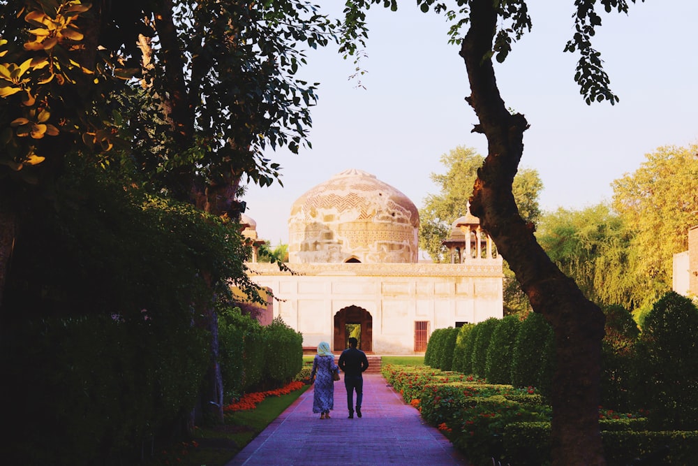 two person walking on pathway going on dome building during daytime