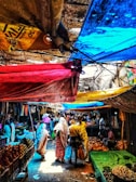 A vibrant street market bursting with colorful fabrics and fresh produce under sunny skies.
