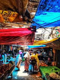 A vibrant street market bustling with people, colors, and fresh produce under soft sunlight.