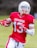 A football player wearing a red jersey with the number 13 and the word 'CRUSADERS' holds a football while running. He is equipped with a white helmet and red gloves, and the background appears to be an outdoor field.
