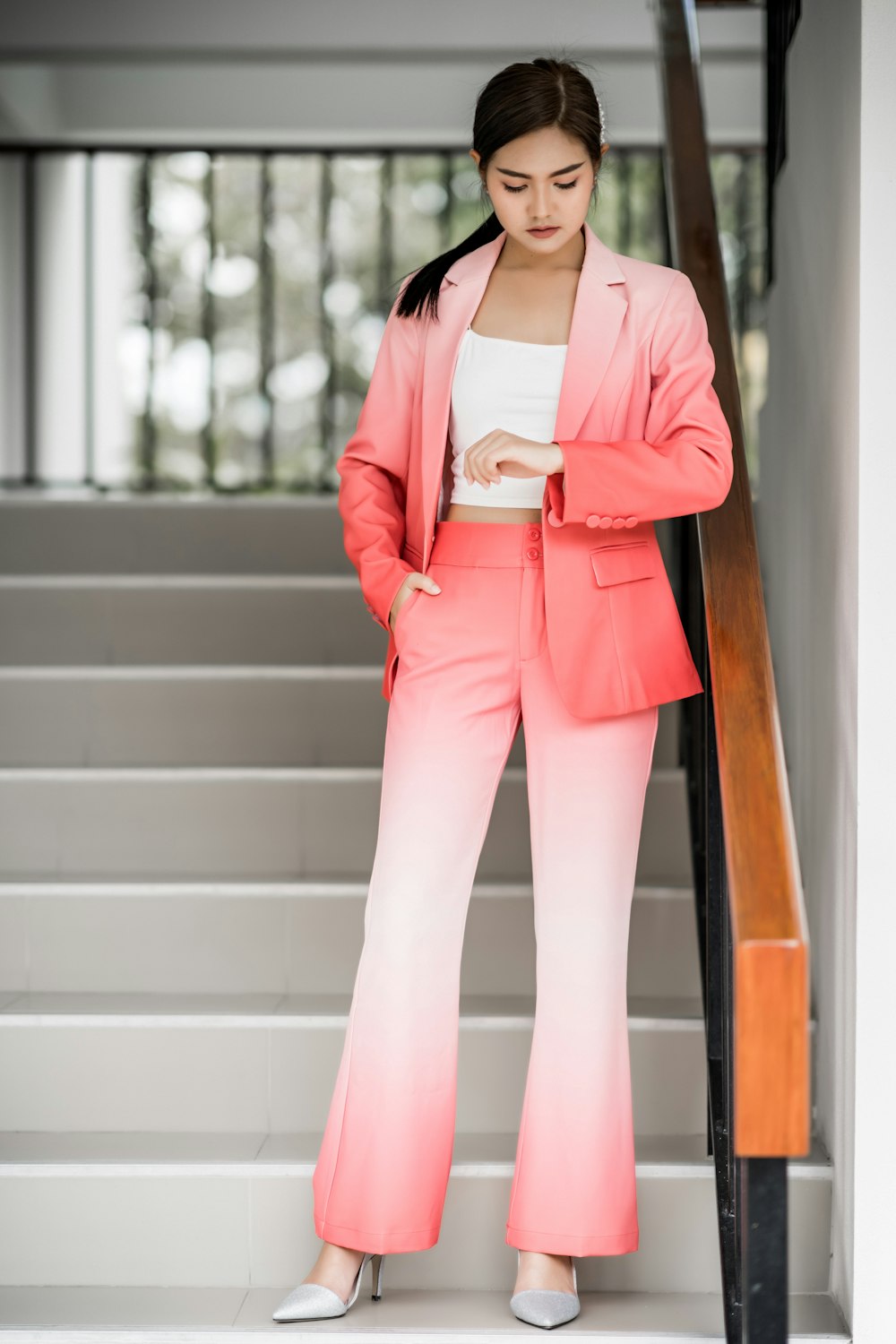 femme portant un blazer et un pantalon ombrés roses et blancs fixant sa montre