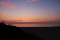 Sunset painting the sky in shades of pink and orange over a peaceful beach cove.