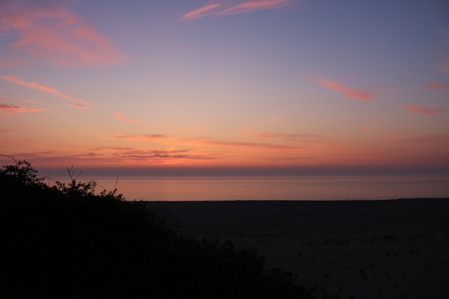 A serene beach at sunset with orange and purple hues in the sky.