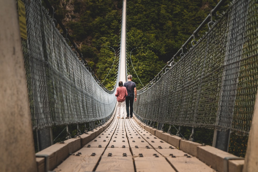 man and woman walking on brown and gray hanging bridge