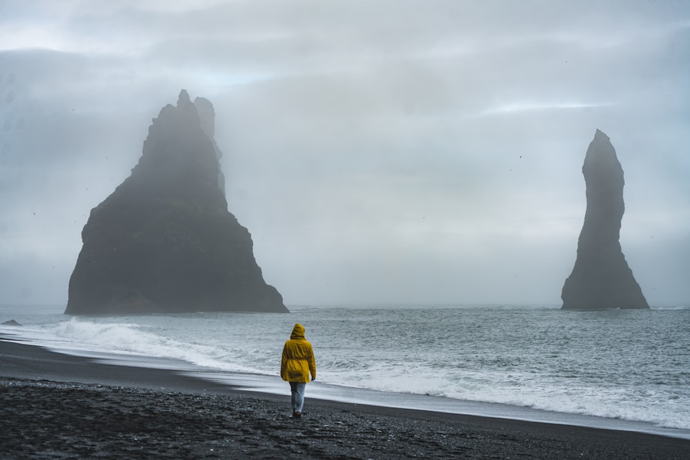 a person in a yellow jacket walking on a beach