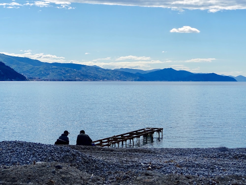 two person sitting near sea dock during cloudy day