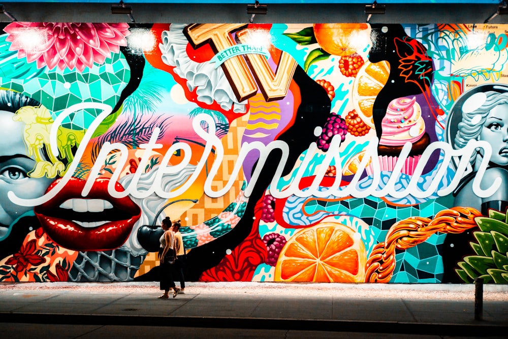 two women walking near multicolored graffiti art
