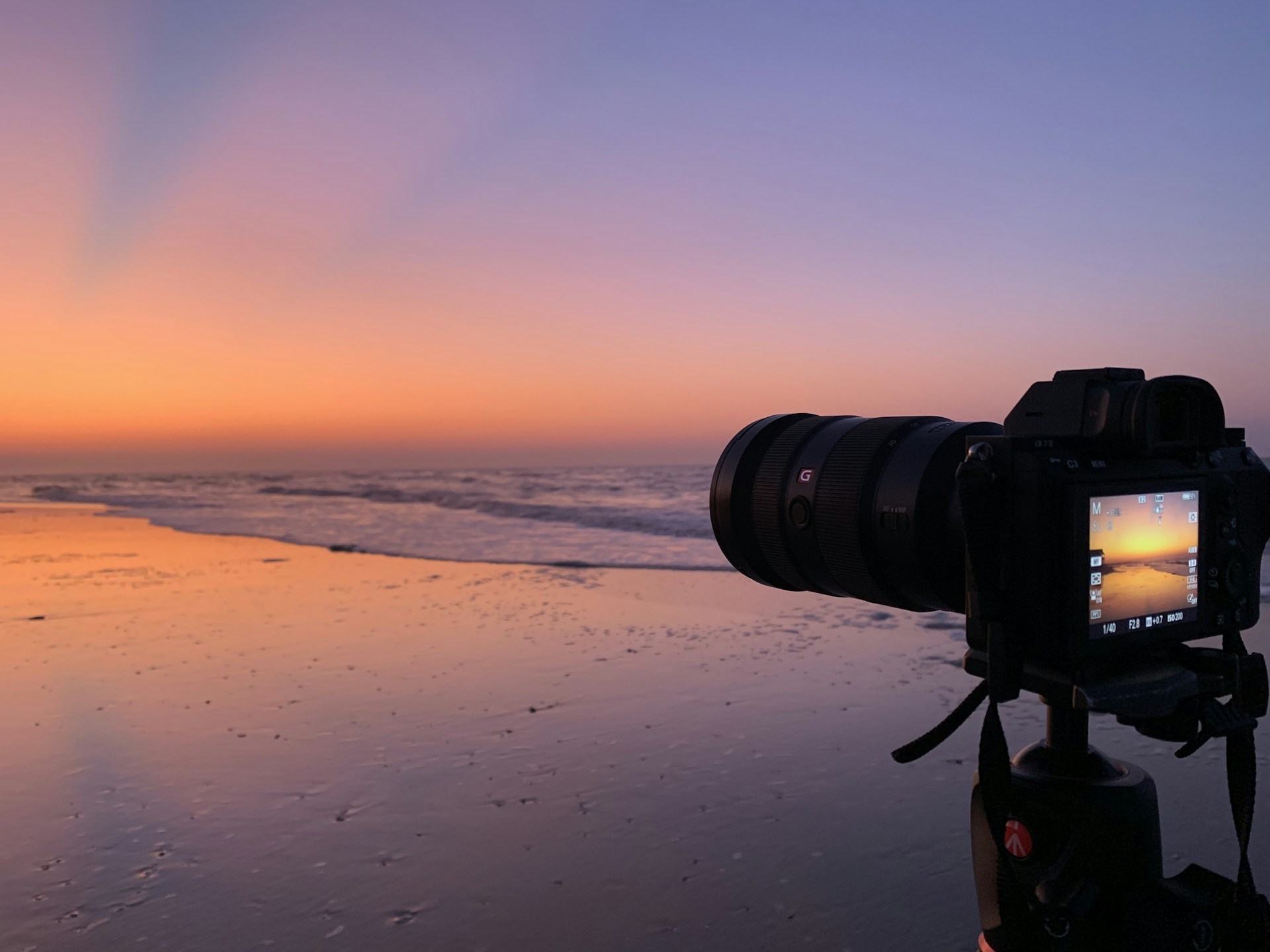 A vibrant photo of a DSLR camera on a tripod capturing a sunset, with ocean waves softly blurred in the background.