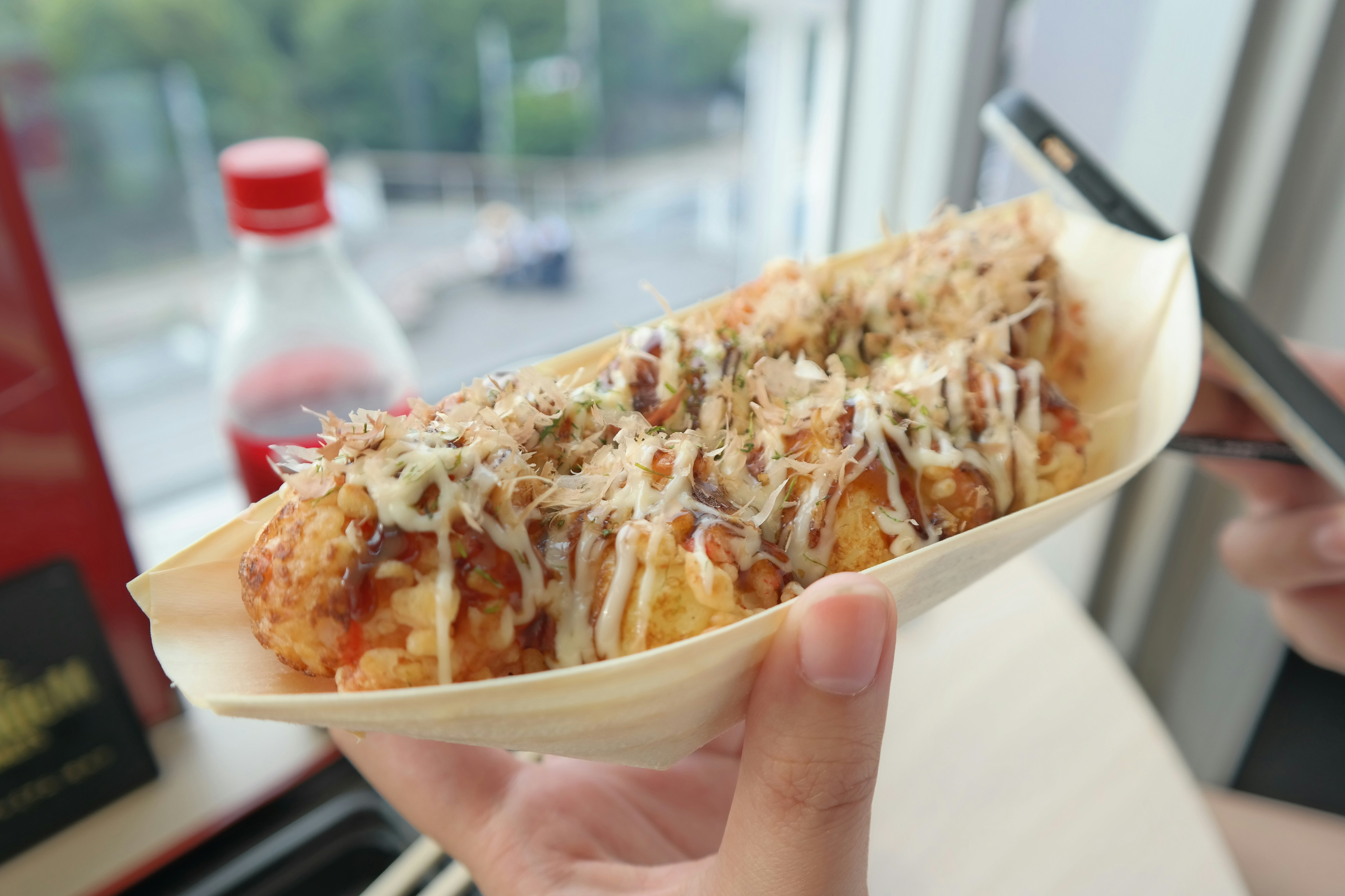 Hand holding a boat of takoyaki with sauce and bonito flakes