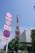 A prominent red and white communications tower stands tall against a clear blue sky. In the foreground, multiple road signs are visible, indicating various traffic regulations. The base of the tower is surrounded by greenery and a modern office building labeled 'Tata Consultancy Services'. The overall scene is urban with clear visibility.